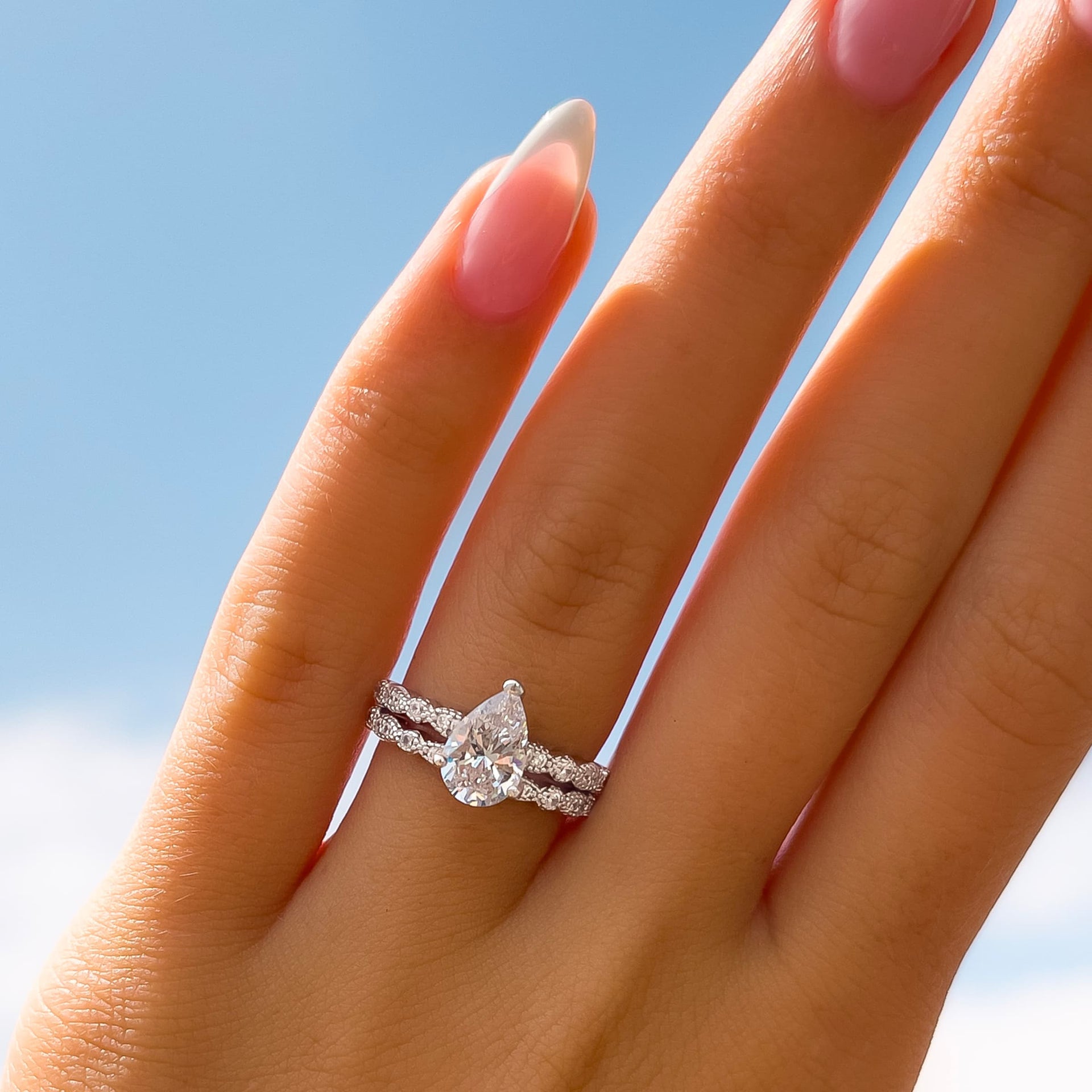 silver vintage pear cut engagement ring paired with matching vintage half eternity band on model with french tip nails with hand up to sky