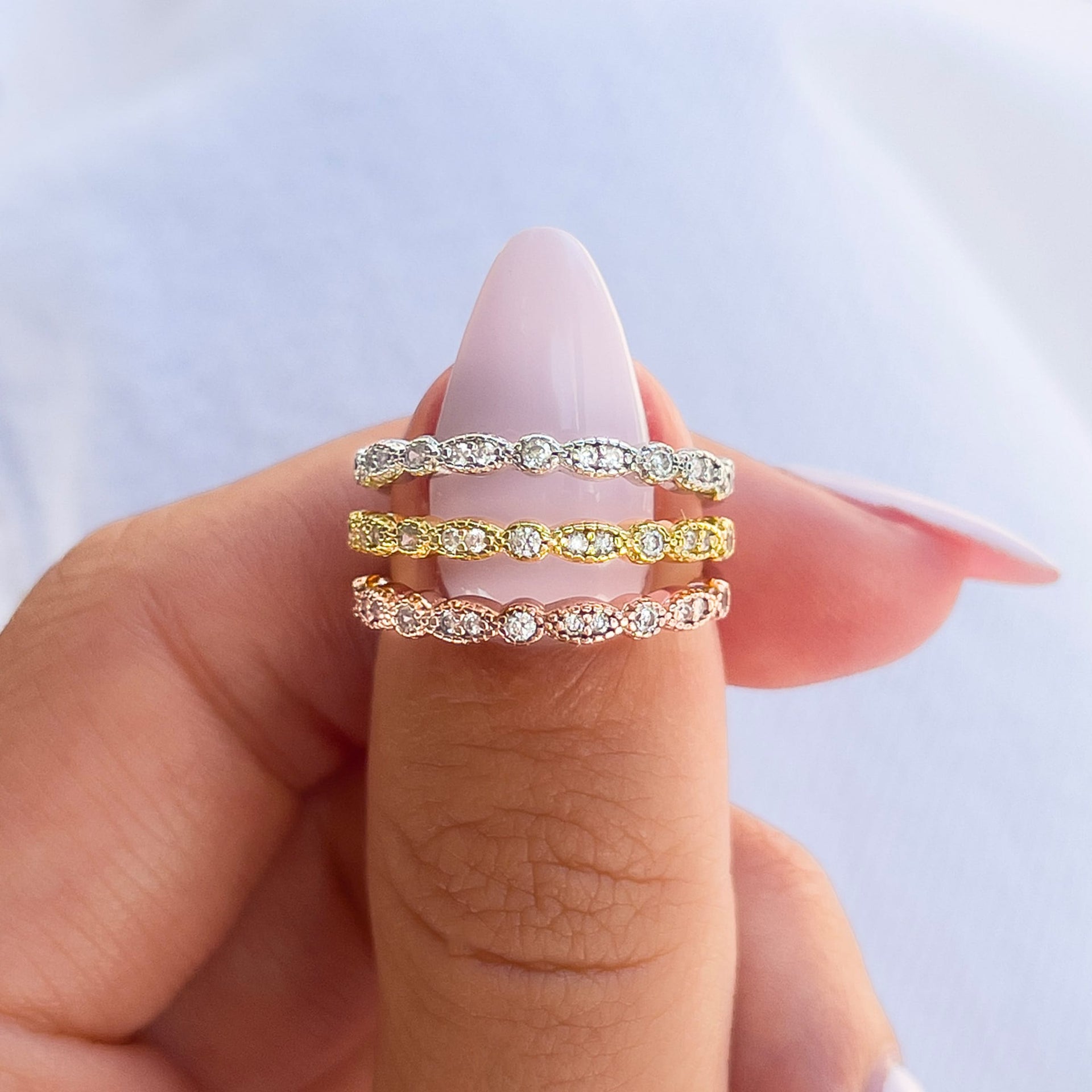 a unique, vintage wedding band shown in silver, gold, and rose gold held by model with light pink nails