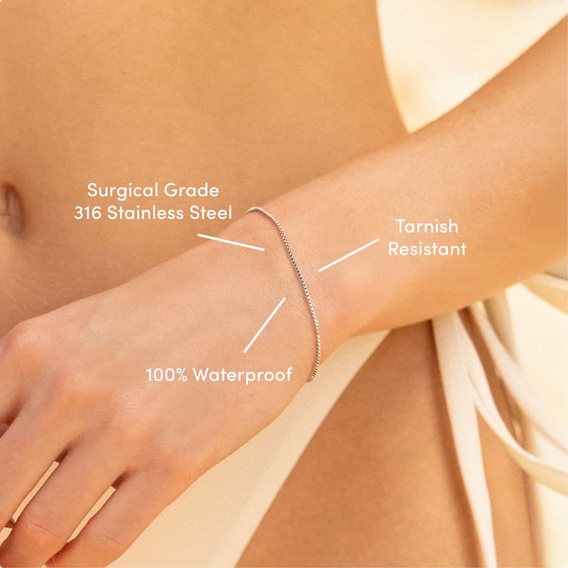 a close up of a simple stainless steel box chain bracelet on a model in an off white bikini with the text overlayed: "surgical grade 316 stainless steel, tarnish resistant, 100% waterproof"